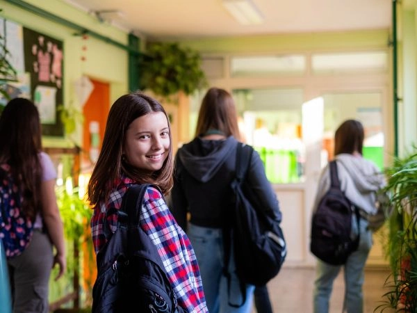 a teenager walking down a corridor at school and smiling for the camera