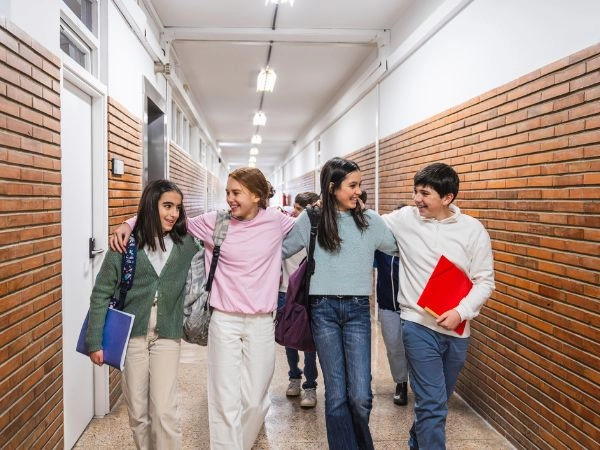 school friends smiling at each other as they walk through the hall carrying textbooks